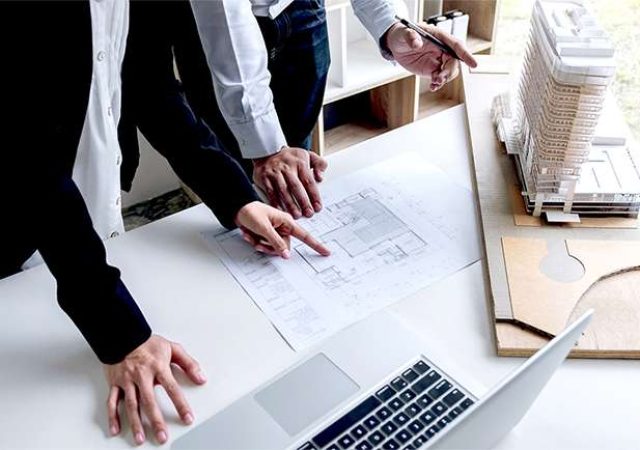 Engineering or Creative architect in construction project Engineers hands working on construction blueprint and building model at a workplace in office Building and architecture concept.